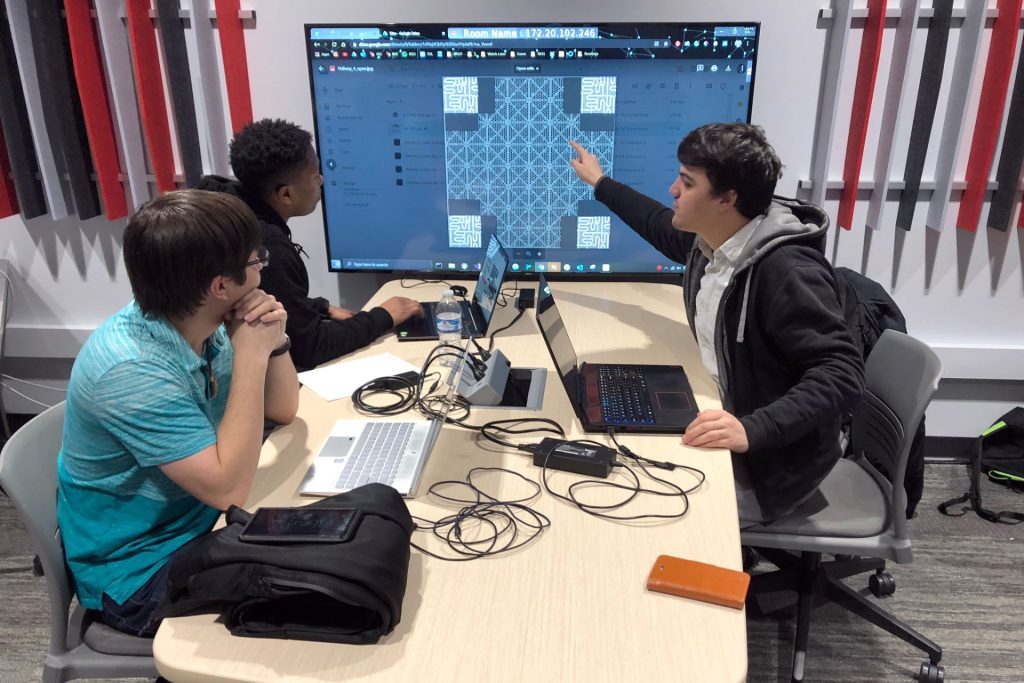 Three students study a large computer screen
