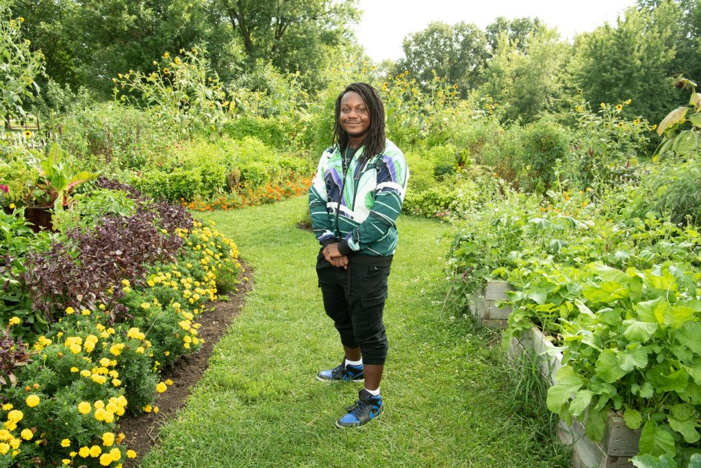student wearing a colorful, green jacket standing in a garden