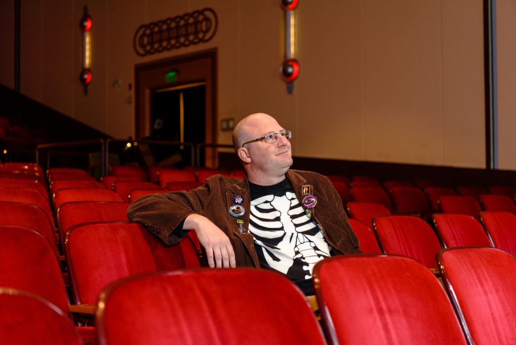 Dr. Eric Wesselmann posing inside Normal Theater, sitting down on red seats.