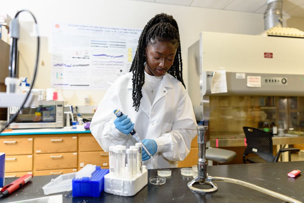 Erinda Aidoo wearing a white lab coat uses a pipet